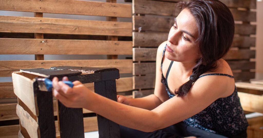 Woman painting wooden crate. Repurposing household items.