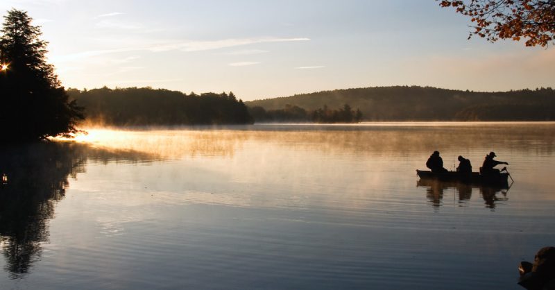 3 people fishing in a boat on a lake