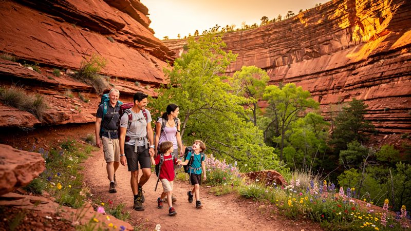 Family hiking a red rock canyon trail near Oklahoma City in spring, surrounded by sandstone cliffs and blooming wildflowers