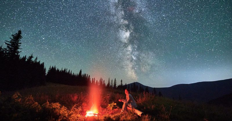 Person sitting by campfire under starlit sky