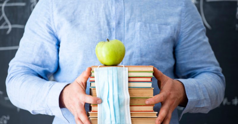 Teacher with books, apple and mask.