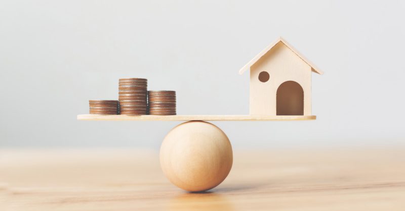 Wooden house and money teetering on a wooden ball
